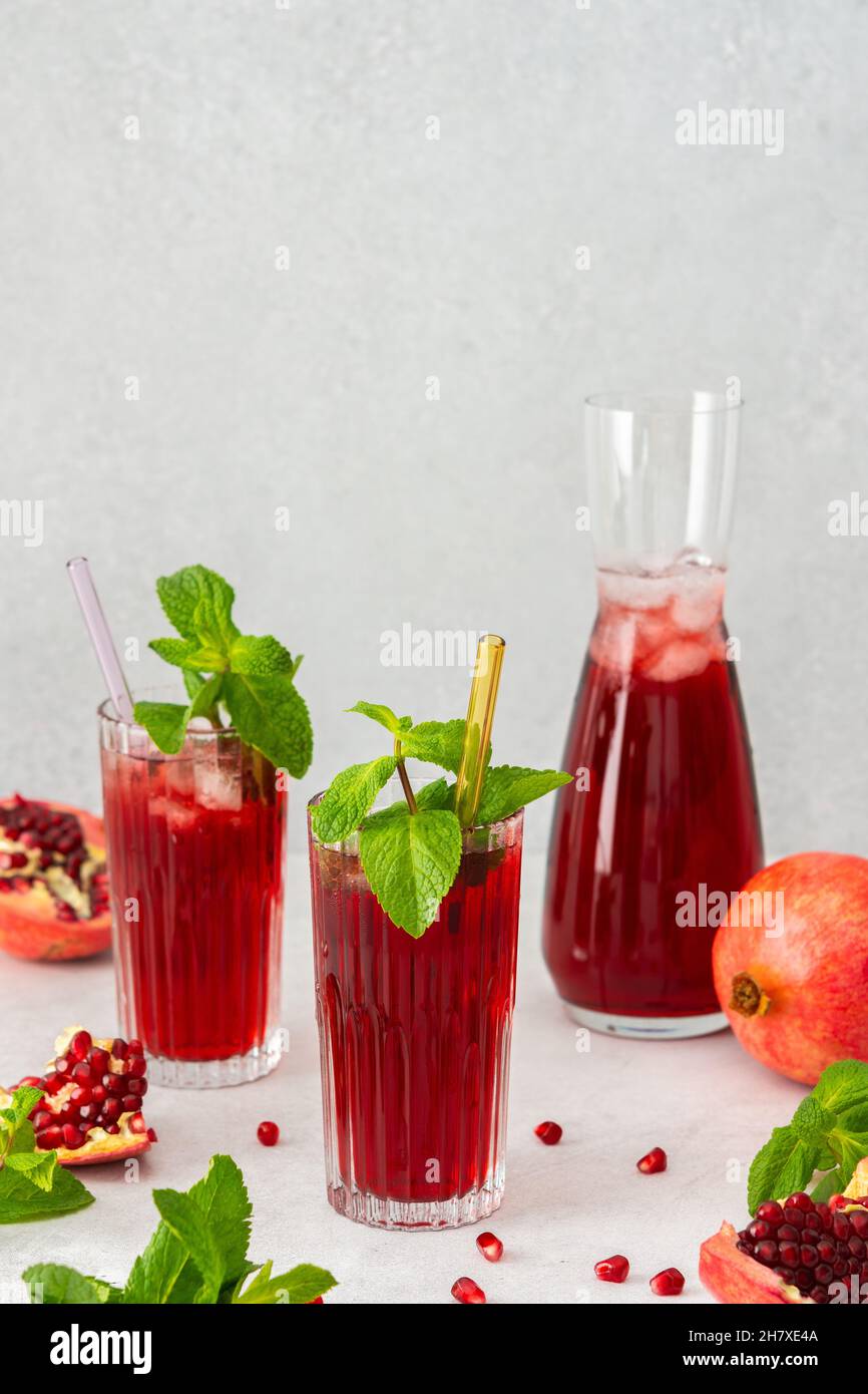 Rinfrescante succo di melograno in bicchieri con paglia di menta e vetro, caraffa di succo di frutta e ghiaccio, bevanda fredda Foto Stock