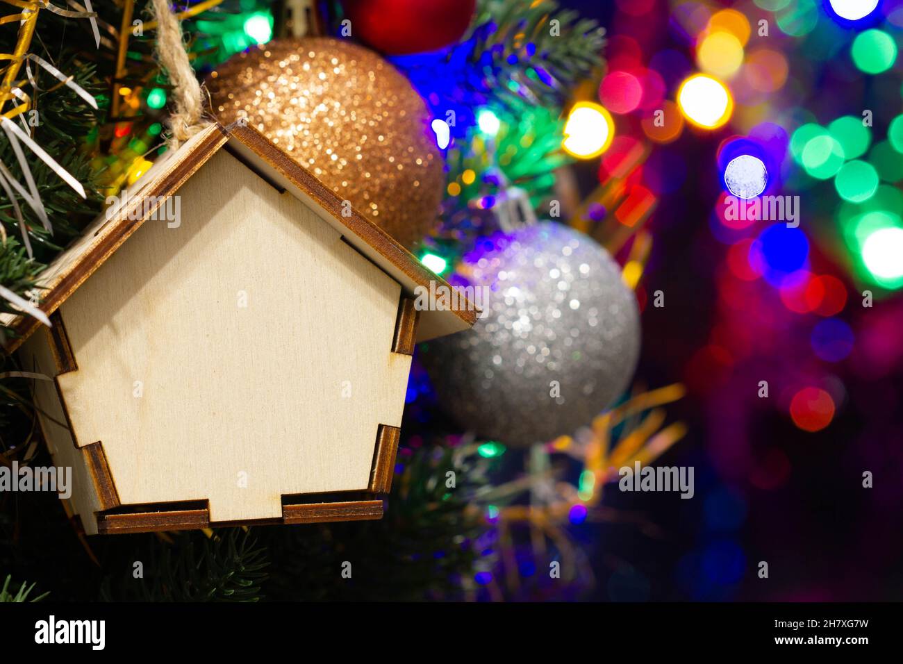 Casa di legno giocattolo di Natale sull'albero di Natale sullo sfondo colorato di illuminazione. Belle decorazioni di Natale. Fantastici giocattoli per l'anno nuovo Foto Stock