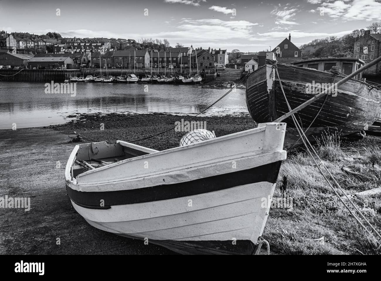 Un dinghy rosso, bianco e blu è ormeggiato su una slitta. Una vecchia barca dilapidata è dietro ed edifici e yacht sono sulla riva lontana. Foto Stock