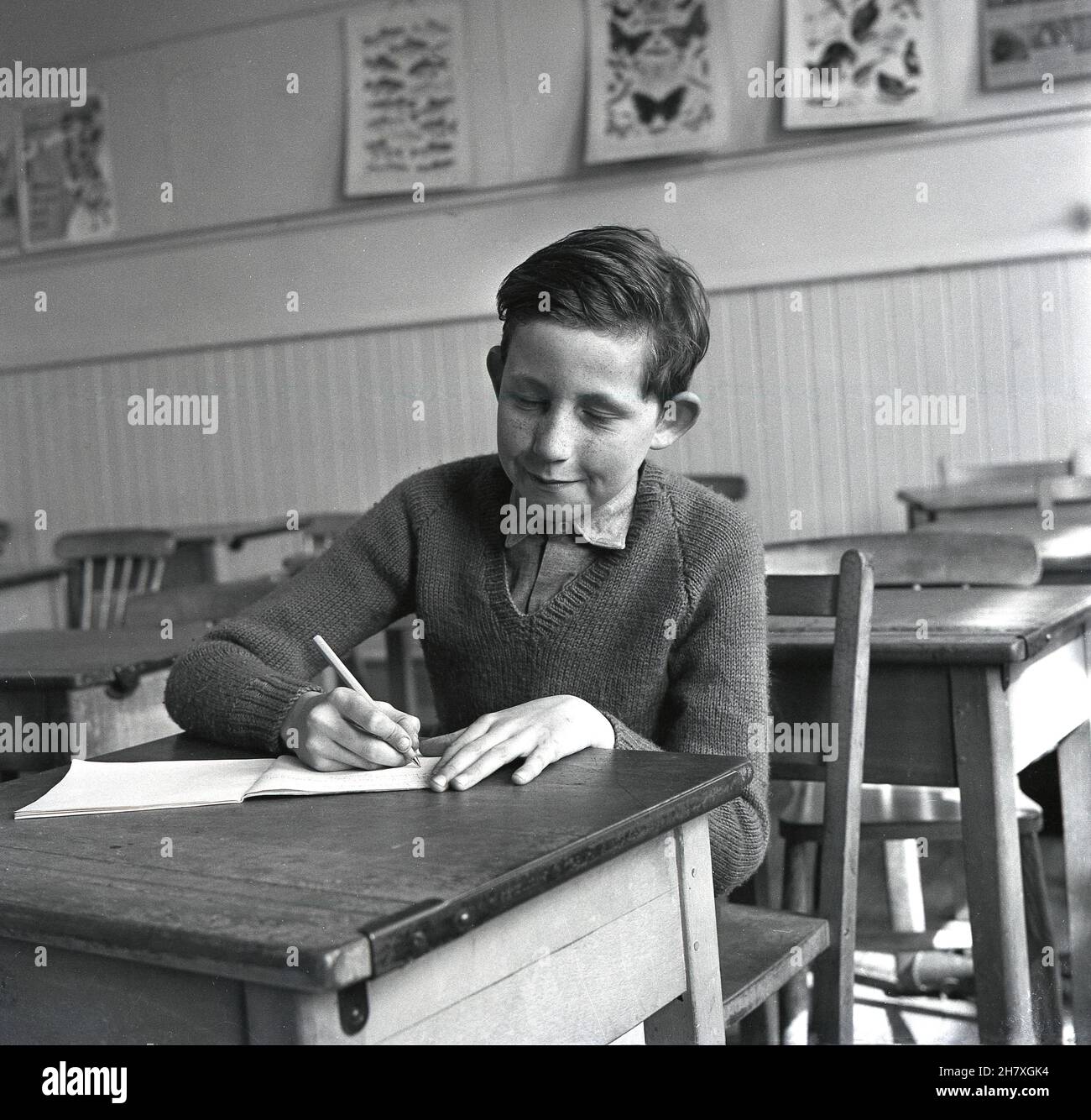 Anni '60, storico, all'interno di una scuola elementare classe, un ragazzo seduto in un tradizionale scrittorio di legno scrittura in un pad, Fife, Scozia, Regno Unito. Foto Stock