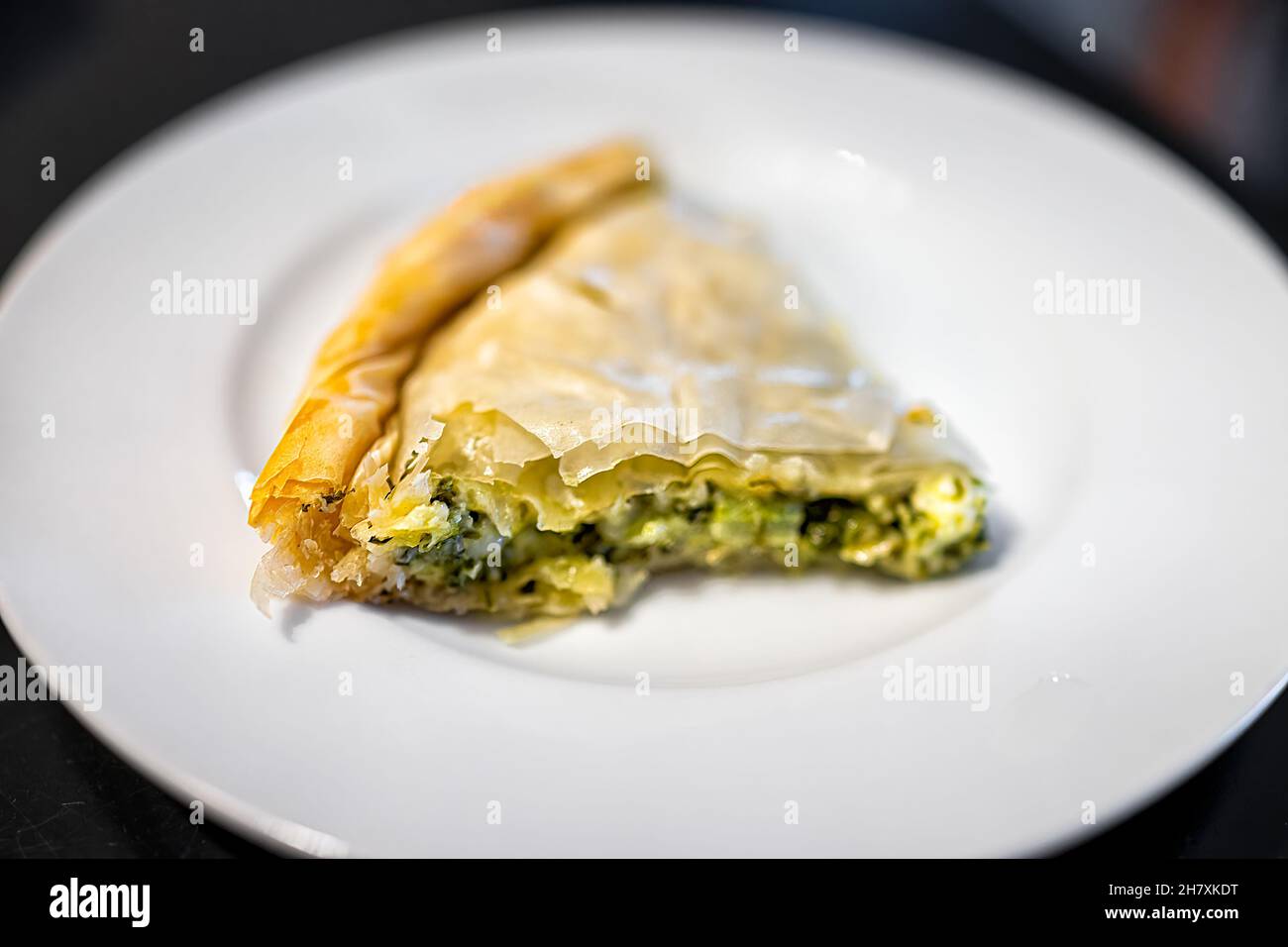 Macro primo piano di pasta filo Spanakopita fetta di torta che serve su piastra bianca isolato sfondo nero come cibo greco tradizionale fatto con spinaci e che Foto Stock