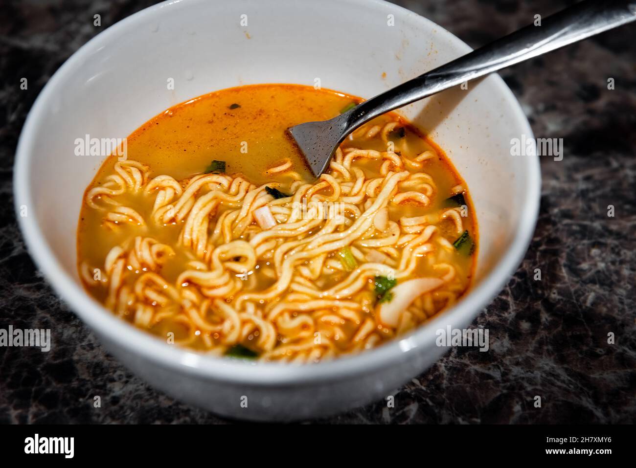 Primo piano di una spaghetti di ramen rosso piccante zuppa istantanea in ciotola con forchetta come pasto asiatico giapponese con consistenza di pasta e cipolle verdi Foto Stock