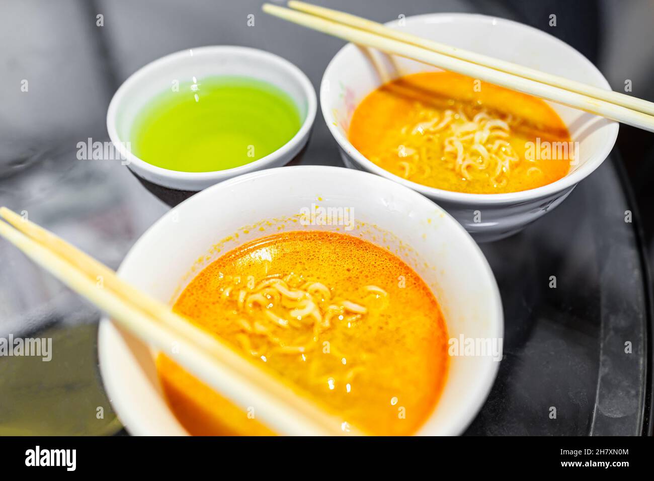 Macrofumatura di due spicciate ciotole rosse ramen zuppa bianca ciotole con bacchette pasto giapponese asiatico e tazza di tè verde Foto Stock