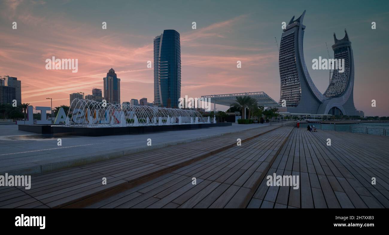 Lusail Corniche presso il porto turistico di Lusail City, il tramonto del Qatar mostra le persone che camminano e si siedono sul lungomare con lo skyline sullo sfondo Foto Stock