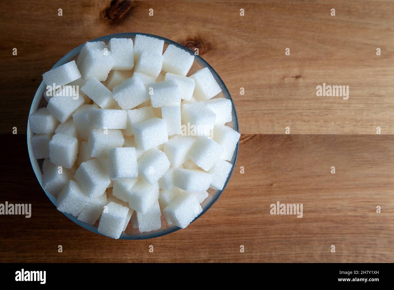 Vista dall'alto dei cubetti di zucchero bianco in una ciotola di vetro, sfondo di legno Foto Stock