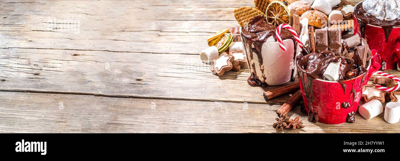 Tazze di cioccolato caldo in stile natalizio con vari condimenti: Fette di cioccolato, spezie, dolci, biscotti, caramelle e pani di zenzero, accogliente in legno Foto Stock