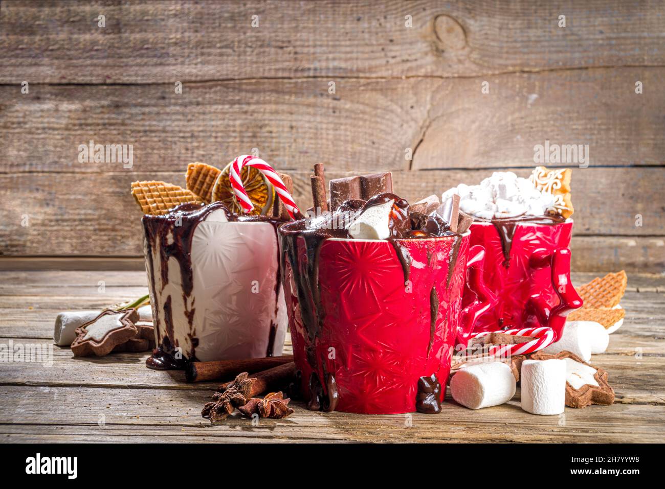 Tazze di cioccolato caldo in stile natalizio con vari condimenti: Fette di cioccolato, spezie, dolci, biscotti, caramelle e pani di zenzero, accogliente in legno Foto Stock