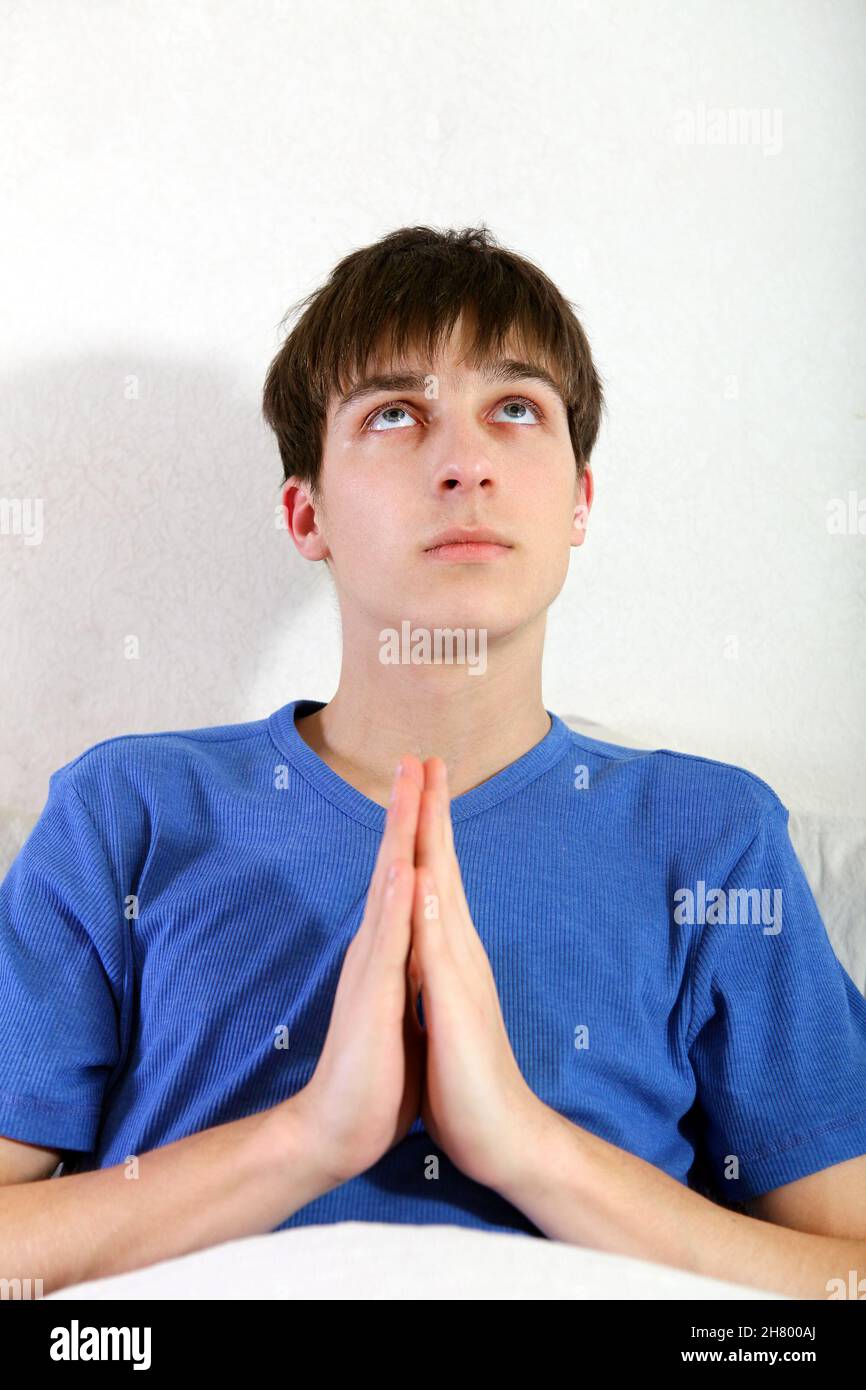 Giovane uomo che prega sul letto a casa Foto Stock