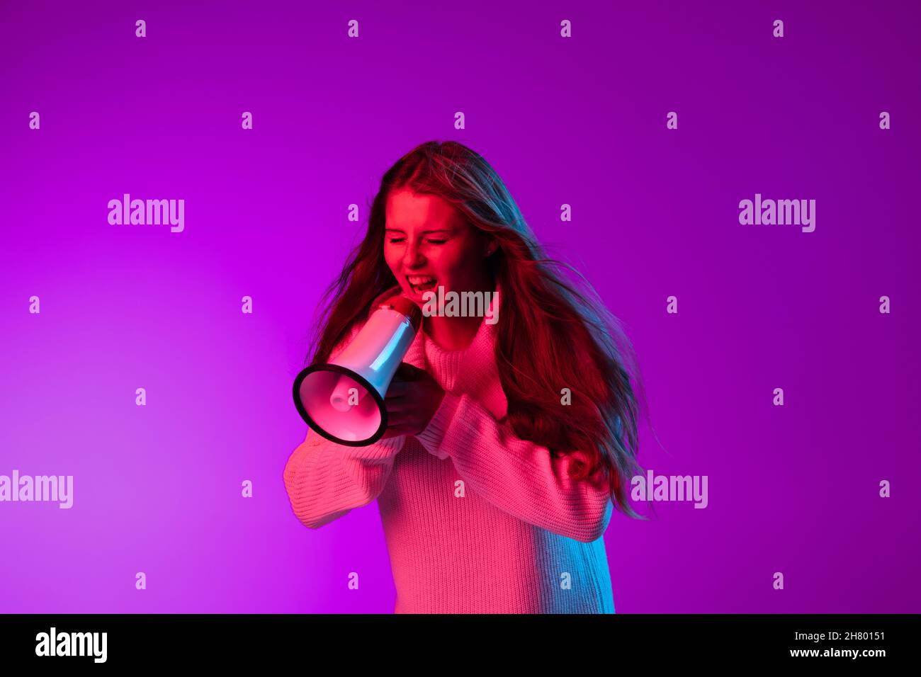 Ritratto di giovane bella ragazza gridando al megaphone isolato su sfondo viola studio in luce neon. Foto Stock