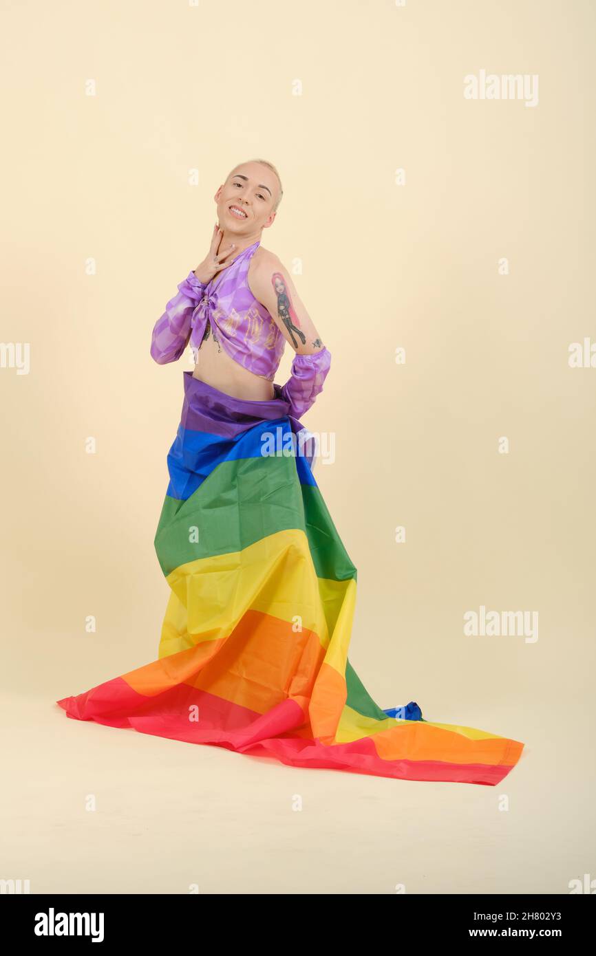 Persona non binaria che guarda la fotocamera e sorride mentre si posa con una bandiera arcobaleno legata intorno alla vita. Foto Stock