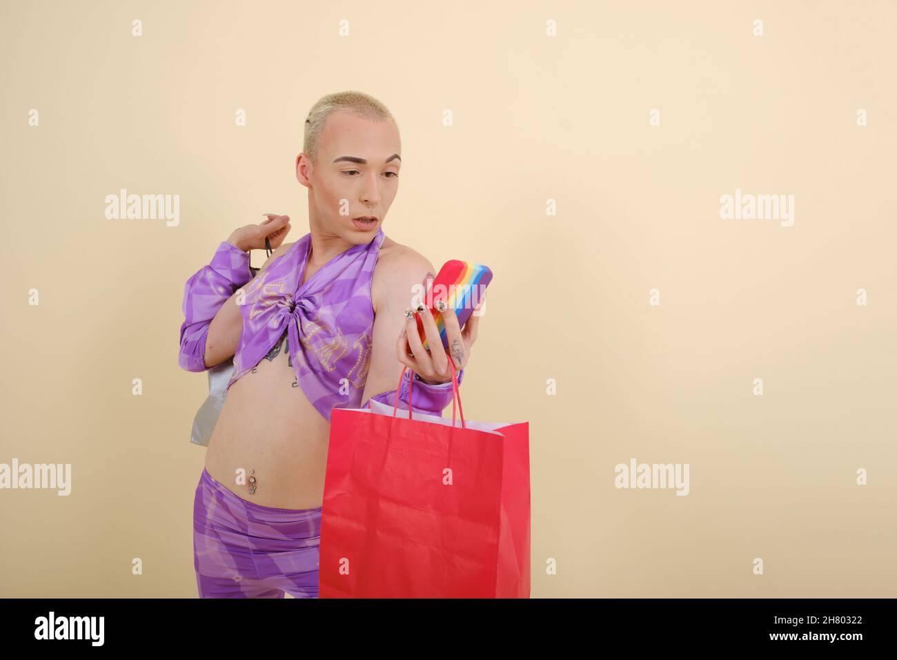 Persona elegante non binaria che utilizza uno smartphone mentre tiene le borse da shopping su uno sfondo isolato. Foto Stock