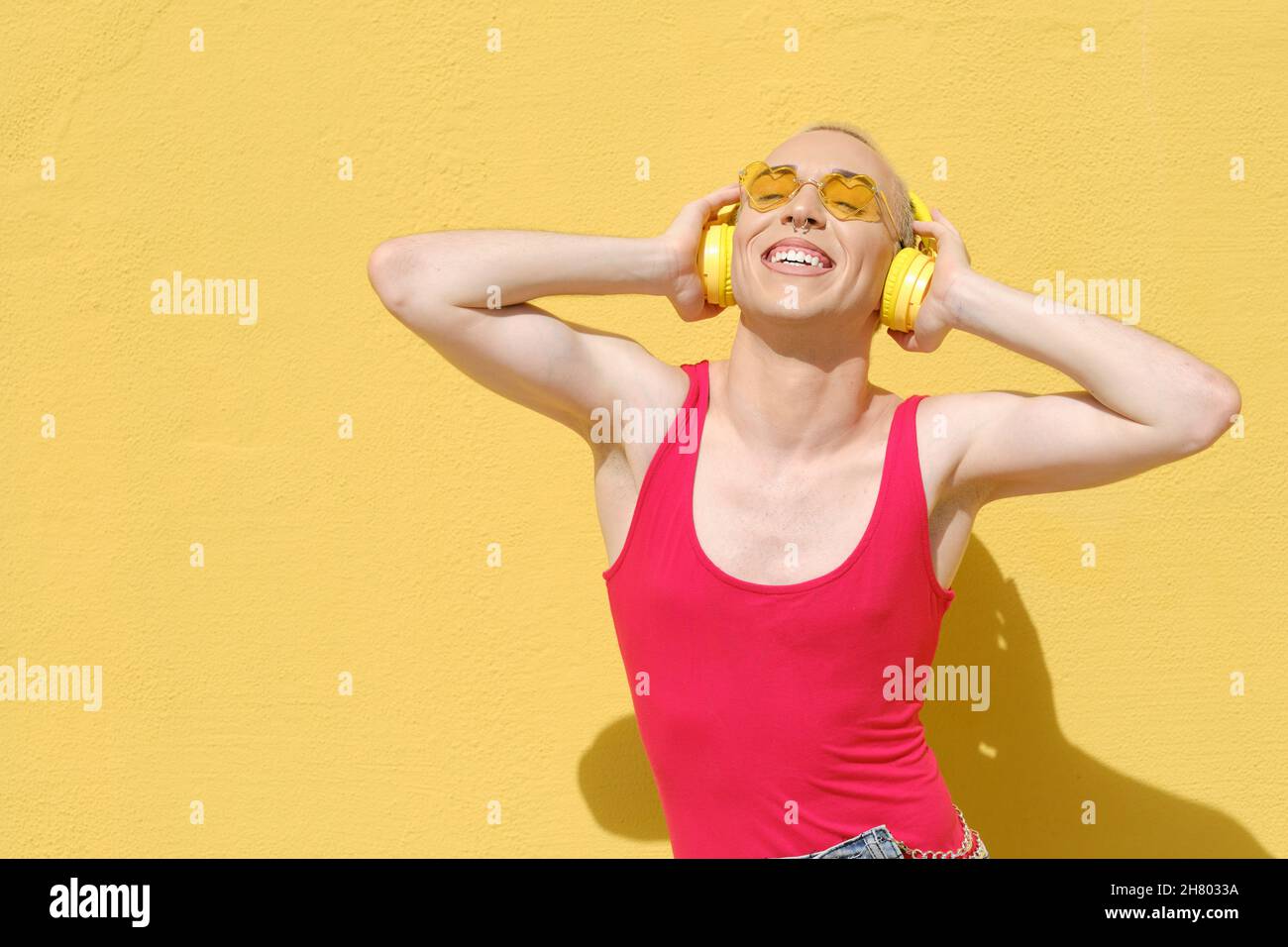 Una persona non binaria sorride mentre ascolti la musica con le cuffie all'aperto. Foto Stock