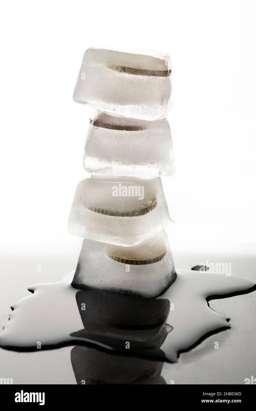 Pila di cubetti di ghiaccio con monete congelate poste su un tavolo nero bagnato con acqua su sfondo bianco in studio chiaro Foto Stock