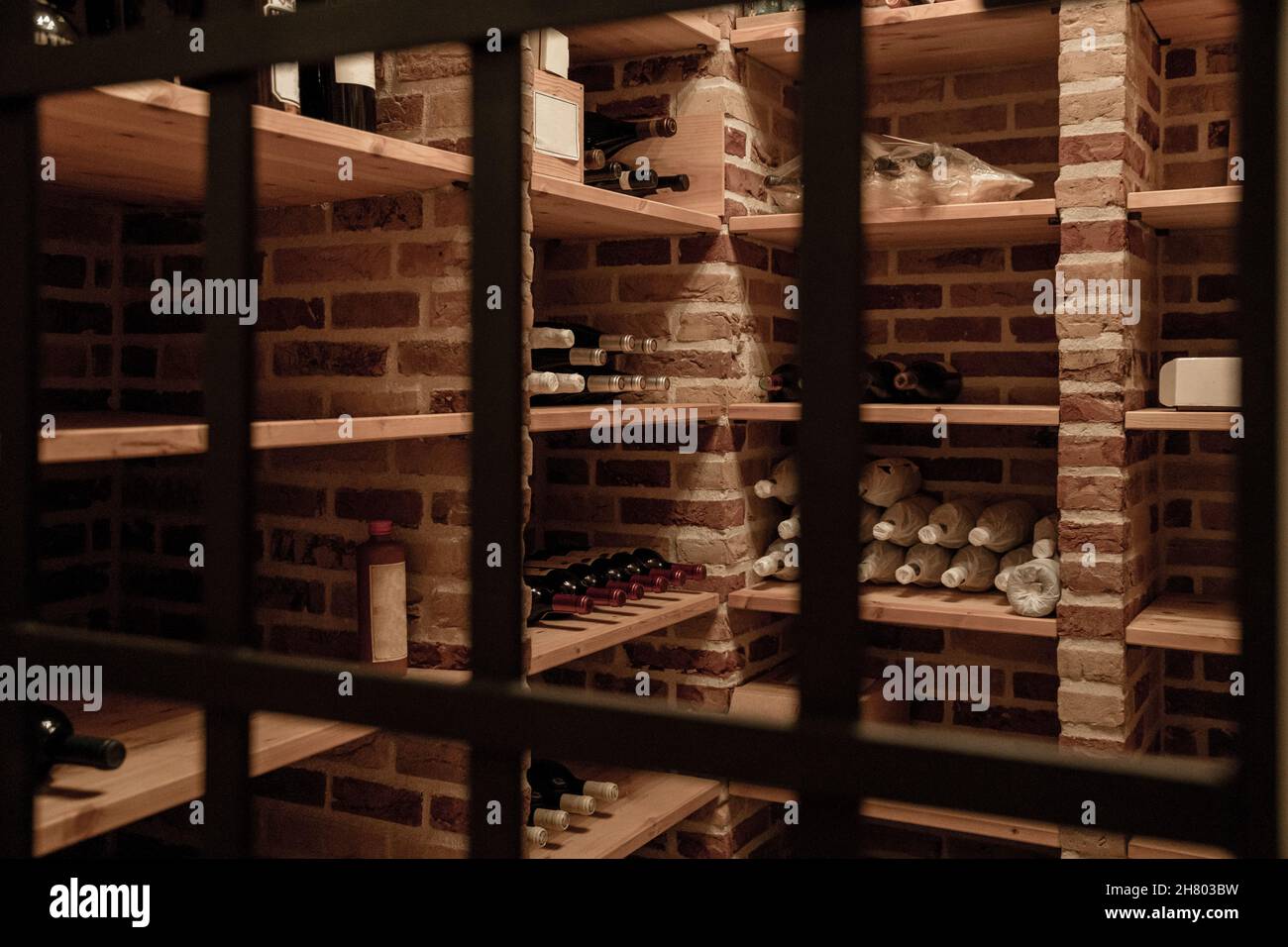 Bottiglie di vino vario poste su mensole in legno in deposito illuminato con pareti in mattoni Foto Stock