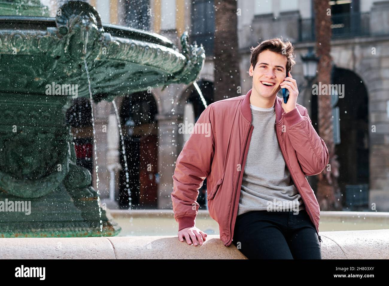 Giovane uomo sorridente mentre parla al telefono all'aperto. Foto Stock