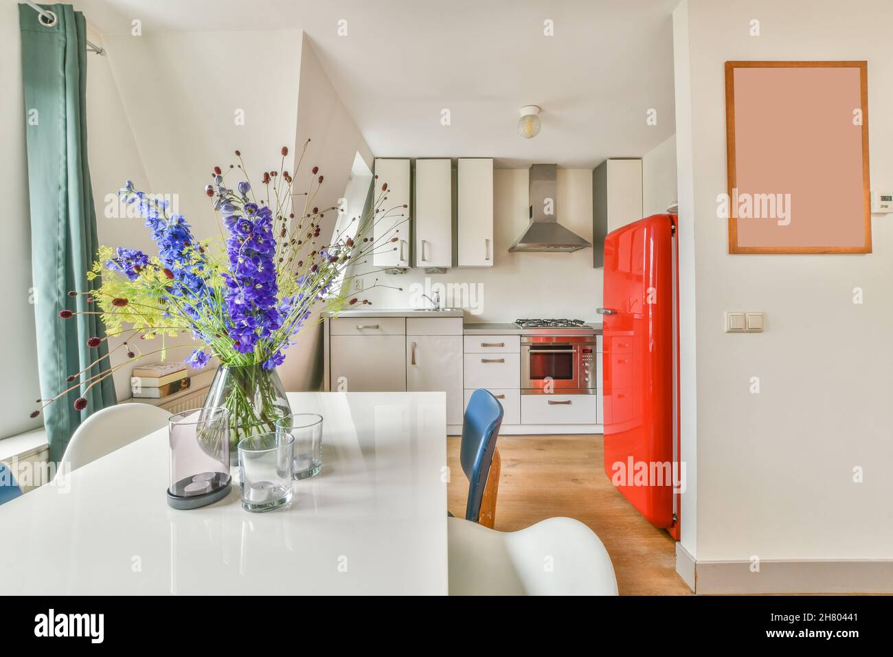 Bancone con lavandino e armadi bianchi vicino al frigorifero rosso vintage in una cucina elegante e luminosa con elettrodomestici moderni e orologio in appartamento Foto Stock