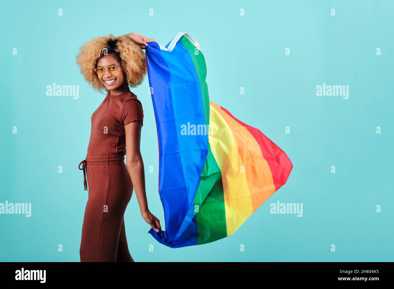 Felice donna afro che detiene una bandiera LGBT orgoglio mentre in piedi su uno sfondo isolato. Foto Stock
