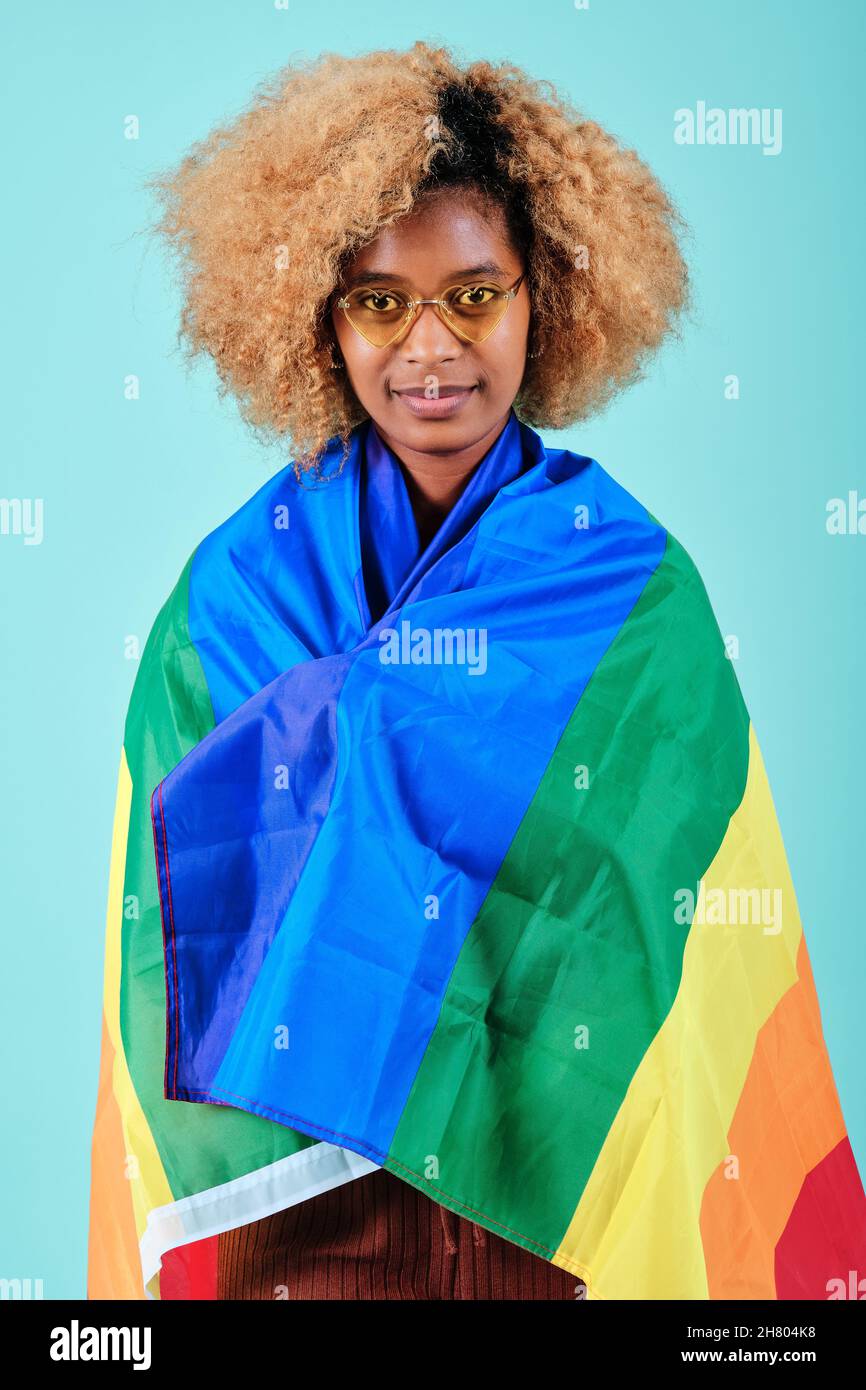 Afro donna che guarda in macchina fotografica mentre avvolto con una bandiera di orgoglio su uno sfondo isolato. Foto Stock