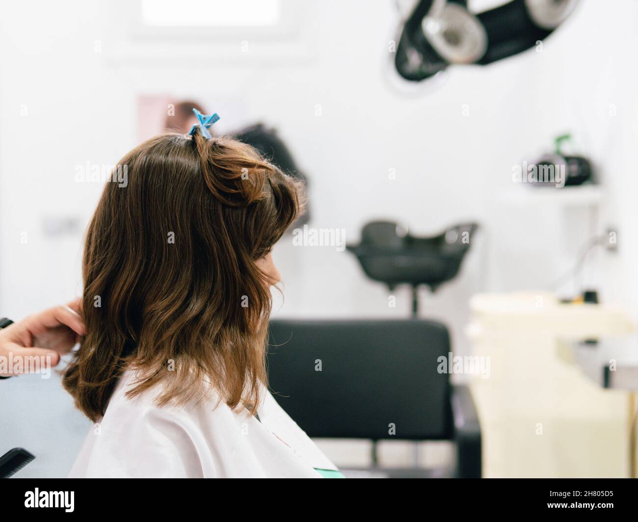 Crop parrucchiere toccare i capelli della ragazza avvolta in cape durante la procedura di acconciatura nel salone professionale Foto Stock