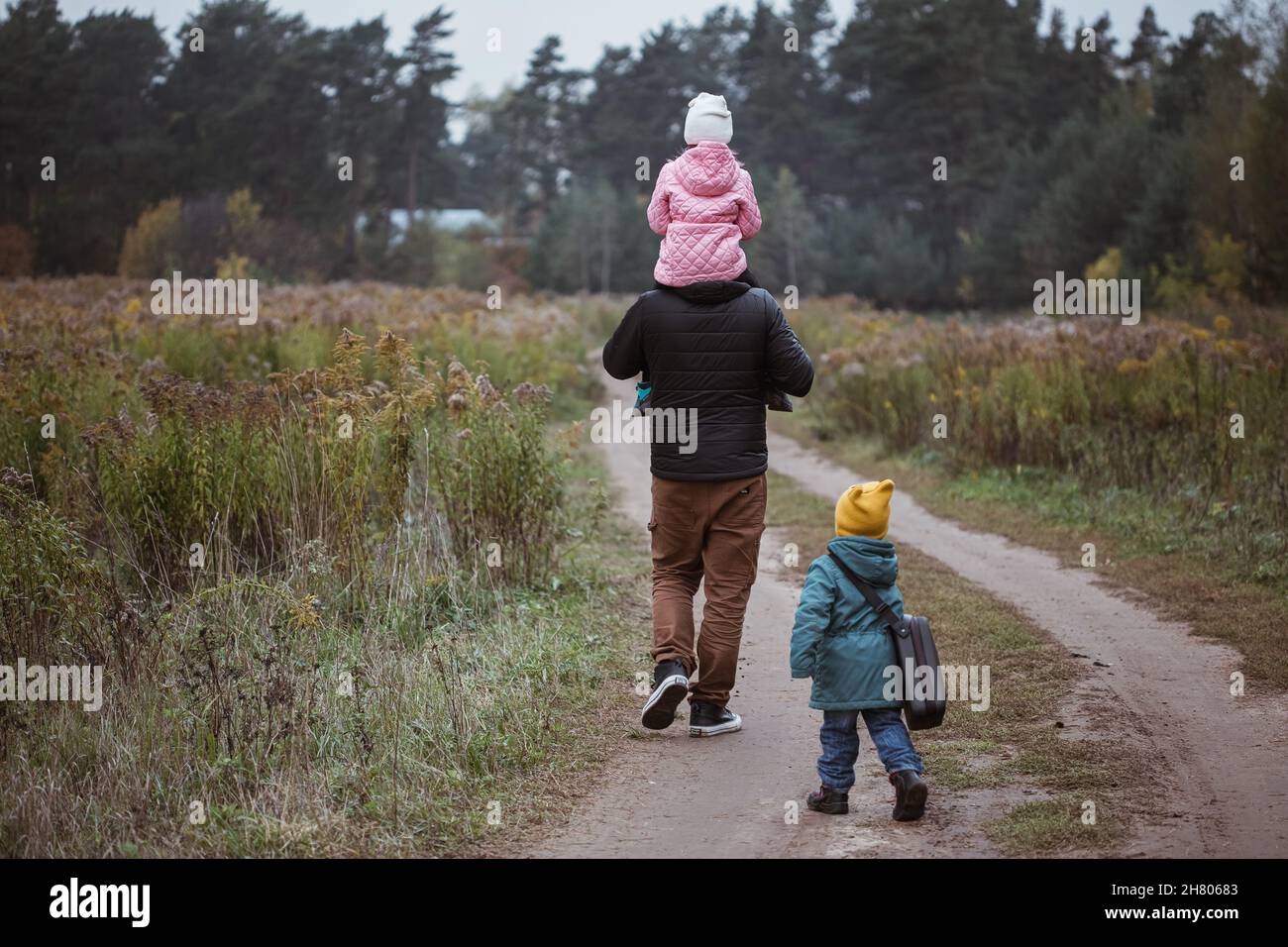 Felice famiglia con due bambini che camminano nel campo autunno tempo. Papà porta la figlia sulle spalle. Foto Stock