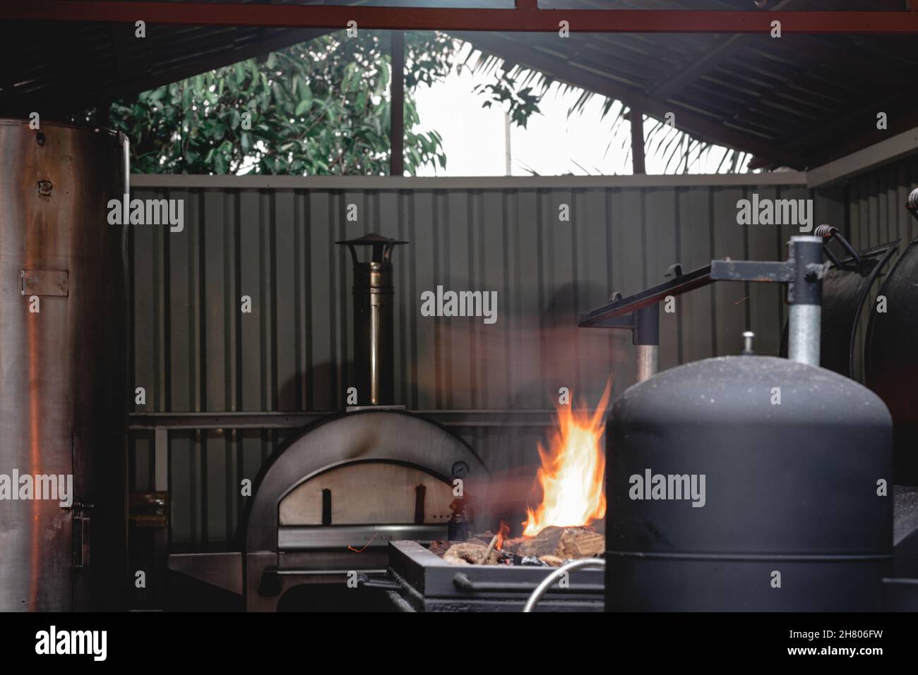 Legno caldo in braciere nero con fiamme e carbone posto vicino alla moderna griglia barbecue sulla terrazza di caffè con pareti Foto Stock