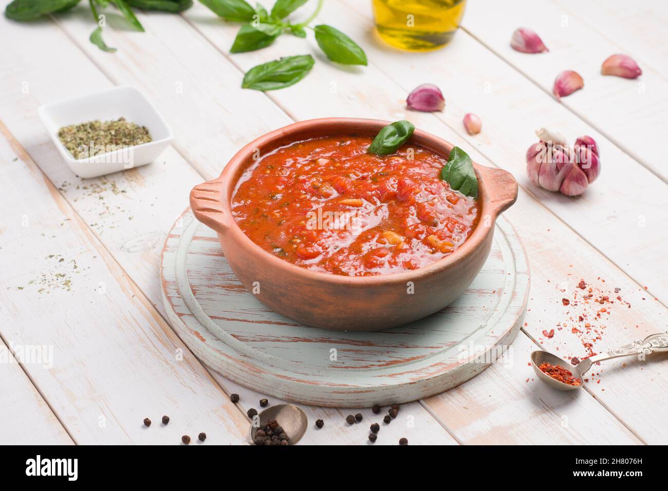 Ciotola di legno di salsa di marinara rossa fatta di pomodoro con foglie di basilico posta su tavola con olio d'oliva e aglio Foto Stock
