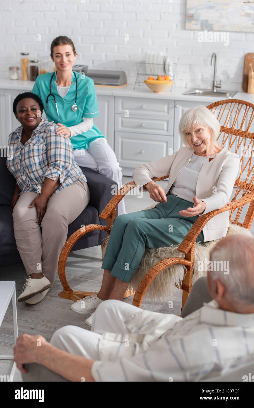 Anziani multietnici che parlano vicino all'infermiere sul divano in casa di cura Foto Stock