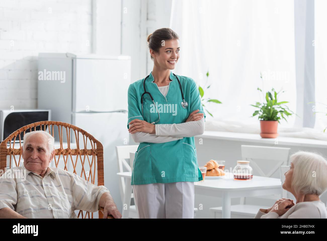 Infermiera positiva in piedi vicino alle persone anziane in casa di cura Foto Stock