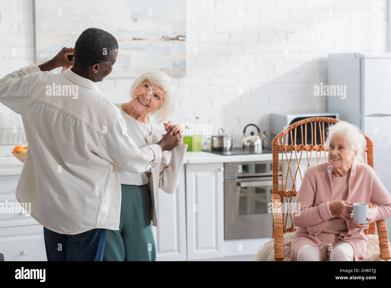 Donna anziana che balla con un amico afroamericano in casa di cura Foto Stock