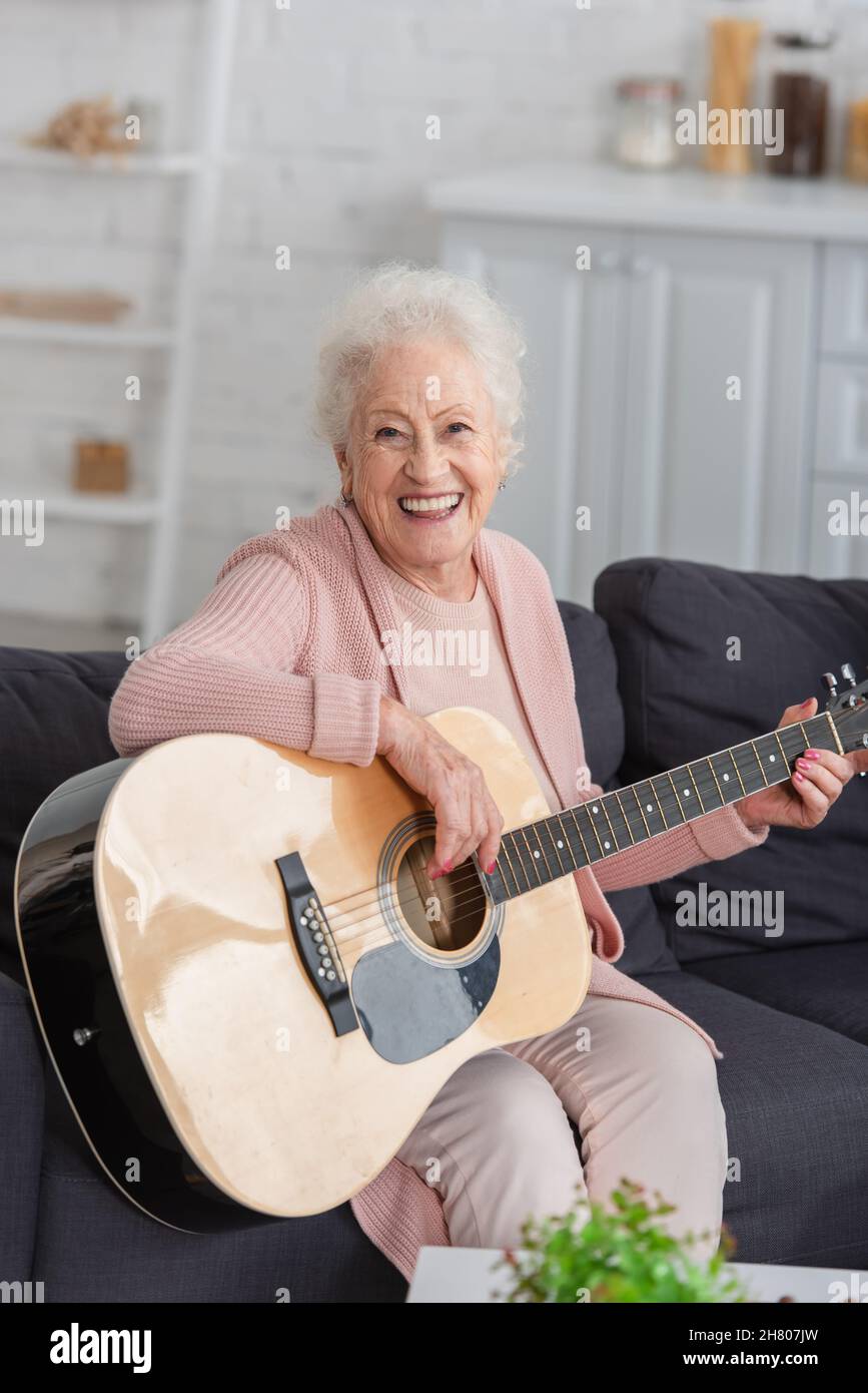 Donna anziana felice che suona la chitarra acustica in casa di cura Foto Stock