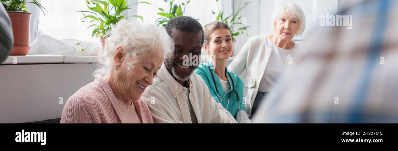 Sorridenti pensionati multietnici e infermiera in casa di cura, banner Foto Stock