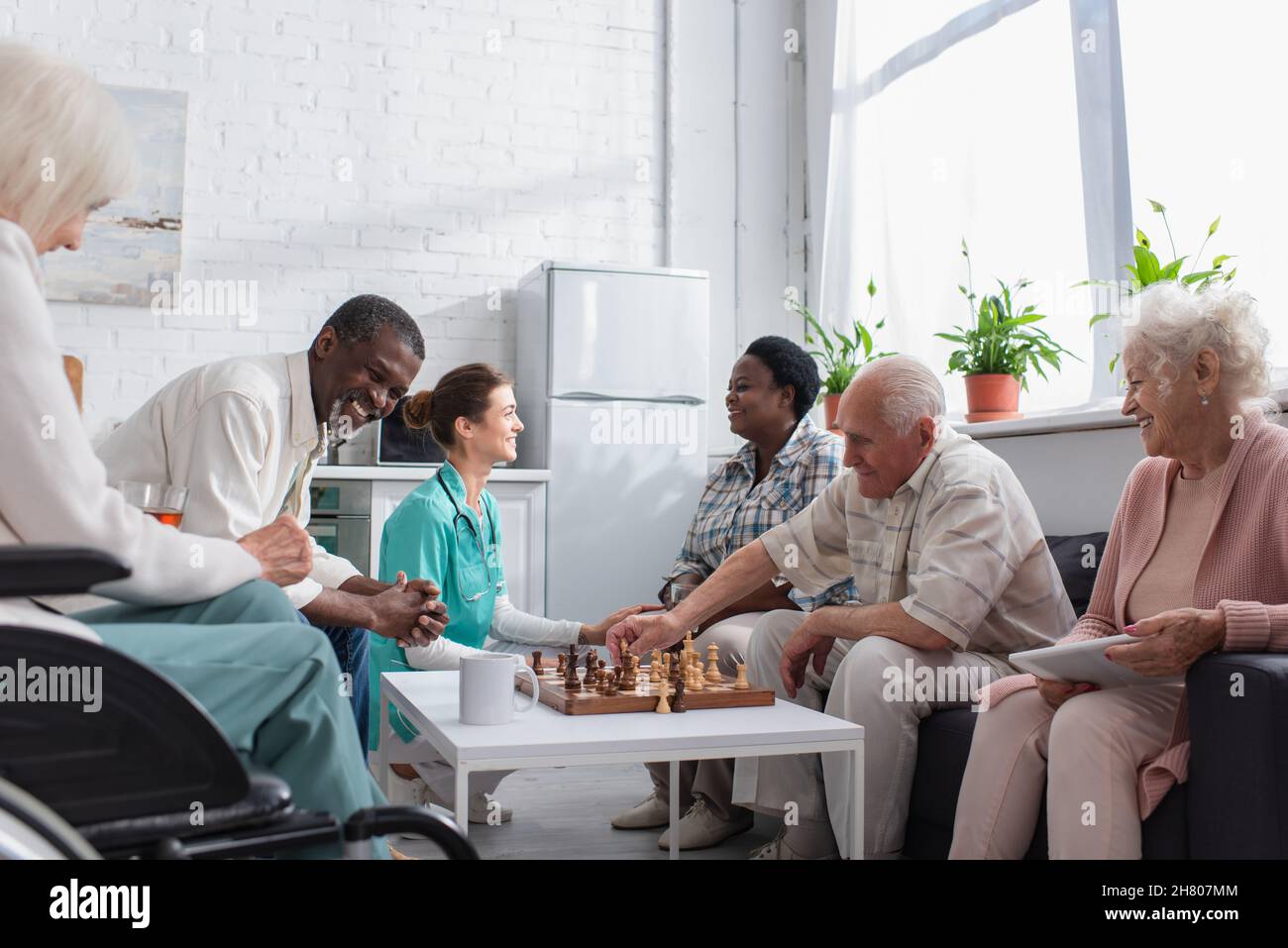 Allegro gente interrazziale che gioca a scacchi vicino infermiera in casa di cura Foto Stock