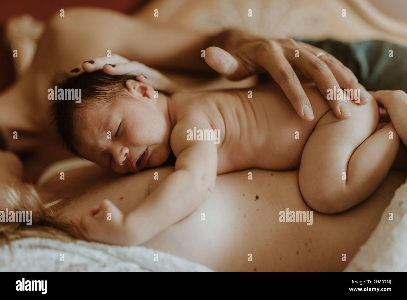 Uomo nudo corto e irriconoscibile che abbraccia la moglie con il neonato mentre si sdraia a letto dopo l'allattamento al seno Foto Stock