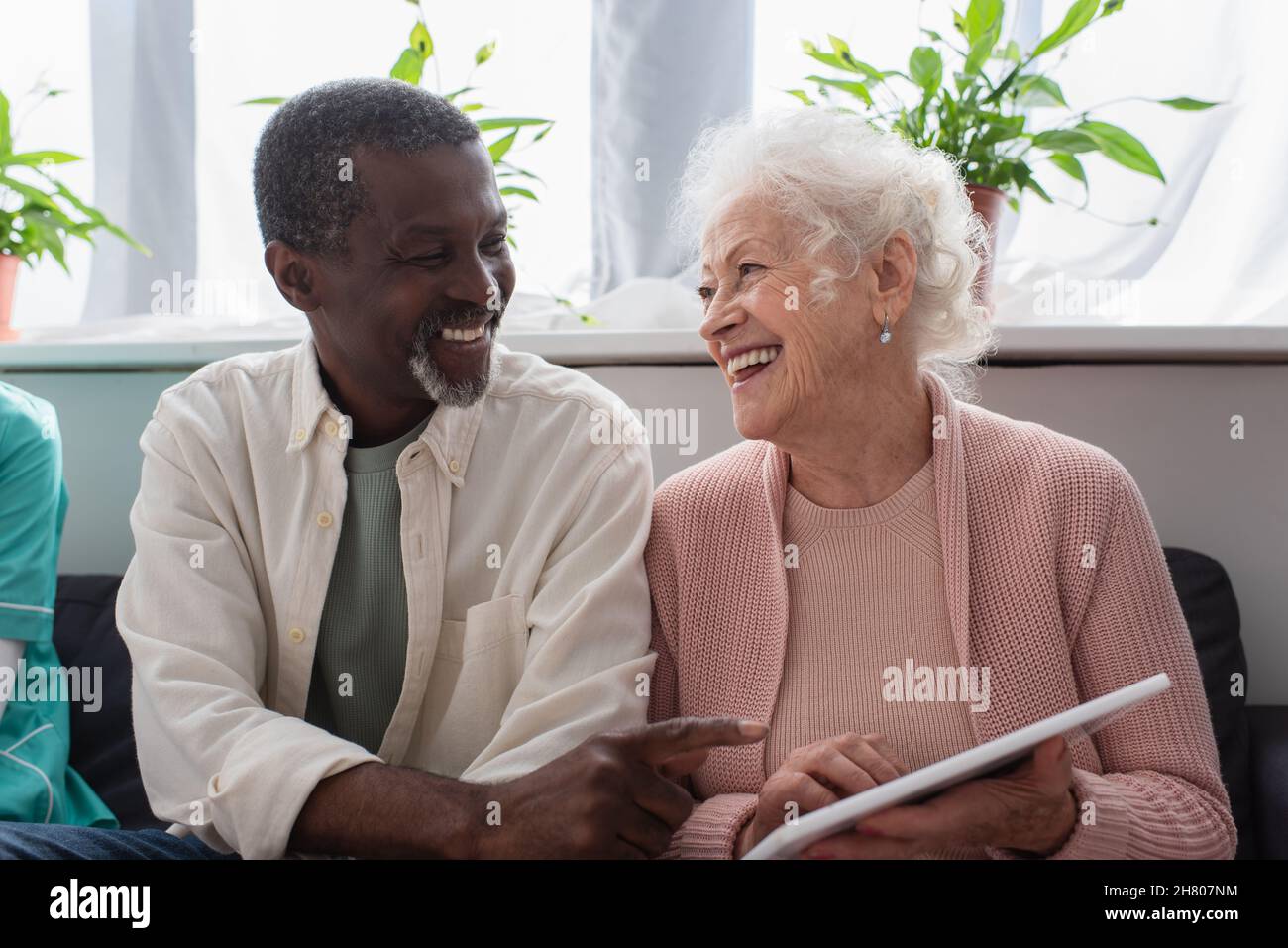 Uomo afroamericano che punta al tablet digitale in mano di un amico anziano in casa di cura Foto Stock