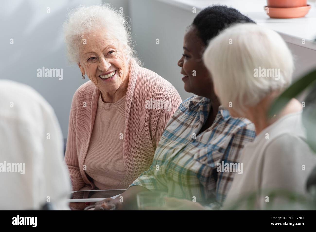 Donne anziane multietniche con tablet digitale che parlano in casa di cura Foto Stock