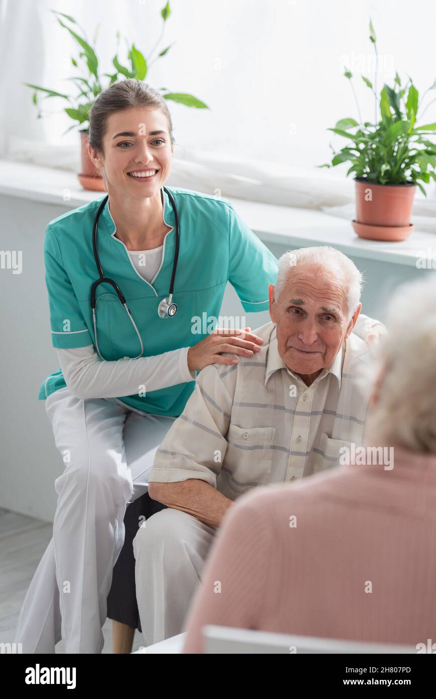 Infermiera felice che abbraccia il paziente anziano nella casa di cura Foto Stock