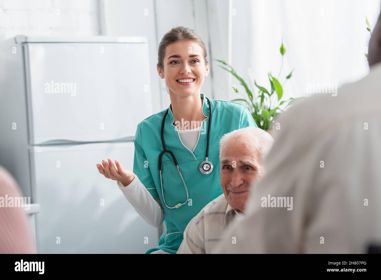Infermiera positiva con stetoscopio vicino a pazienti anziani interrazziali in casa di cura Foto Stock