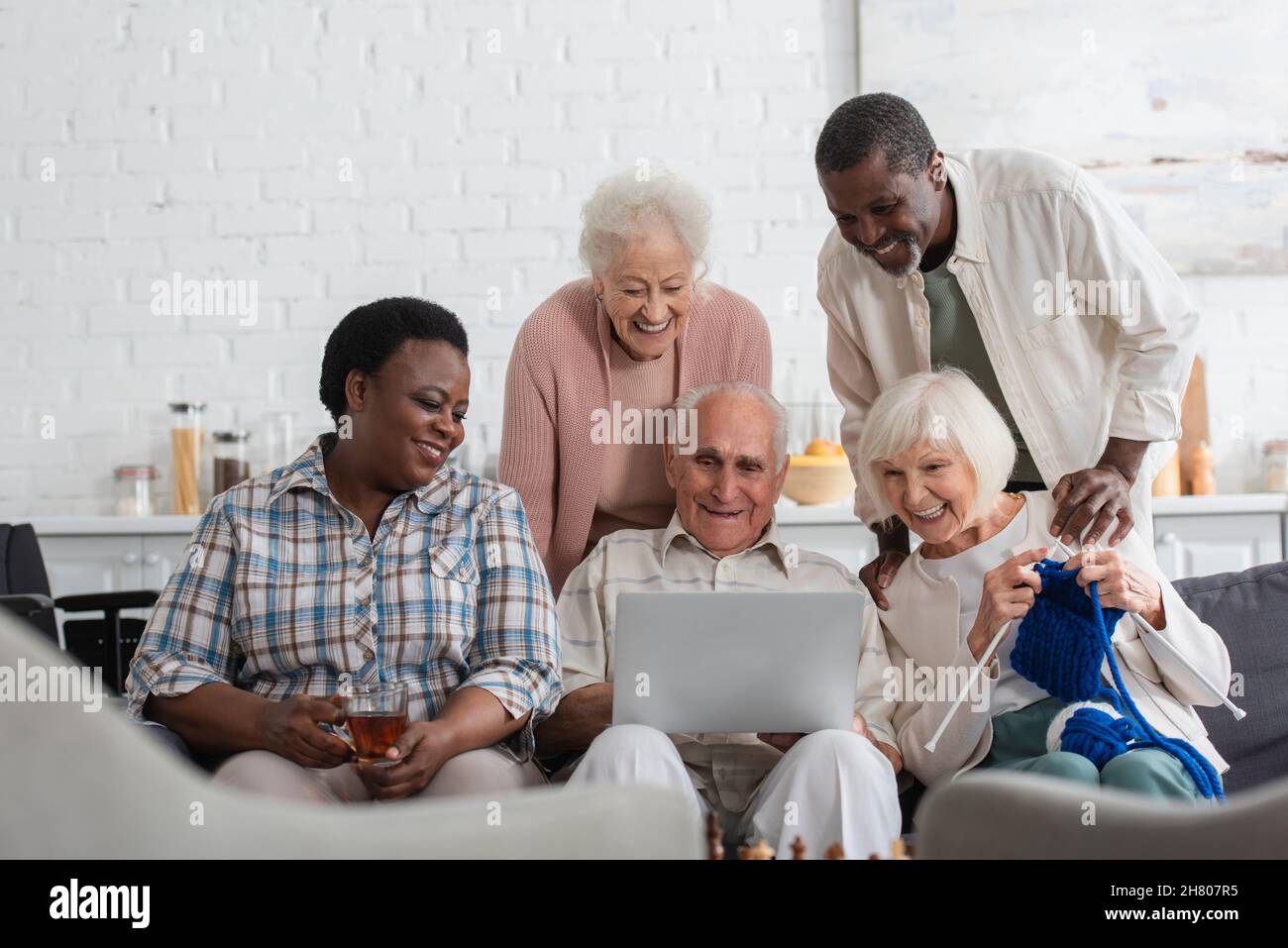 Allegri pensionati interrazziali con filo e tè guardando il computer portatile in casa di cura Foto Stock