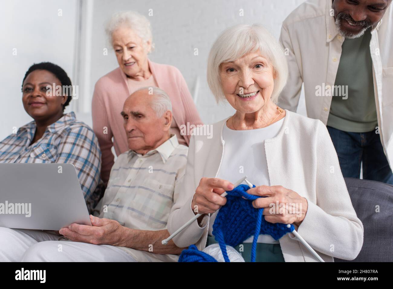Donna anziana che tiene il filo vicino ad amici multietnici con il laptop in casa di cura Foto Stock