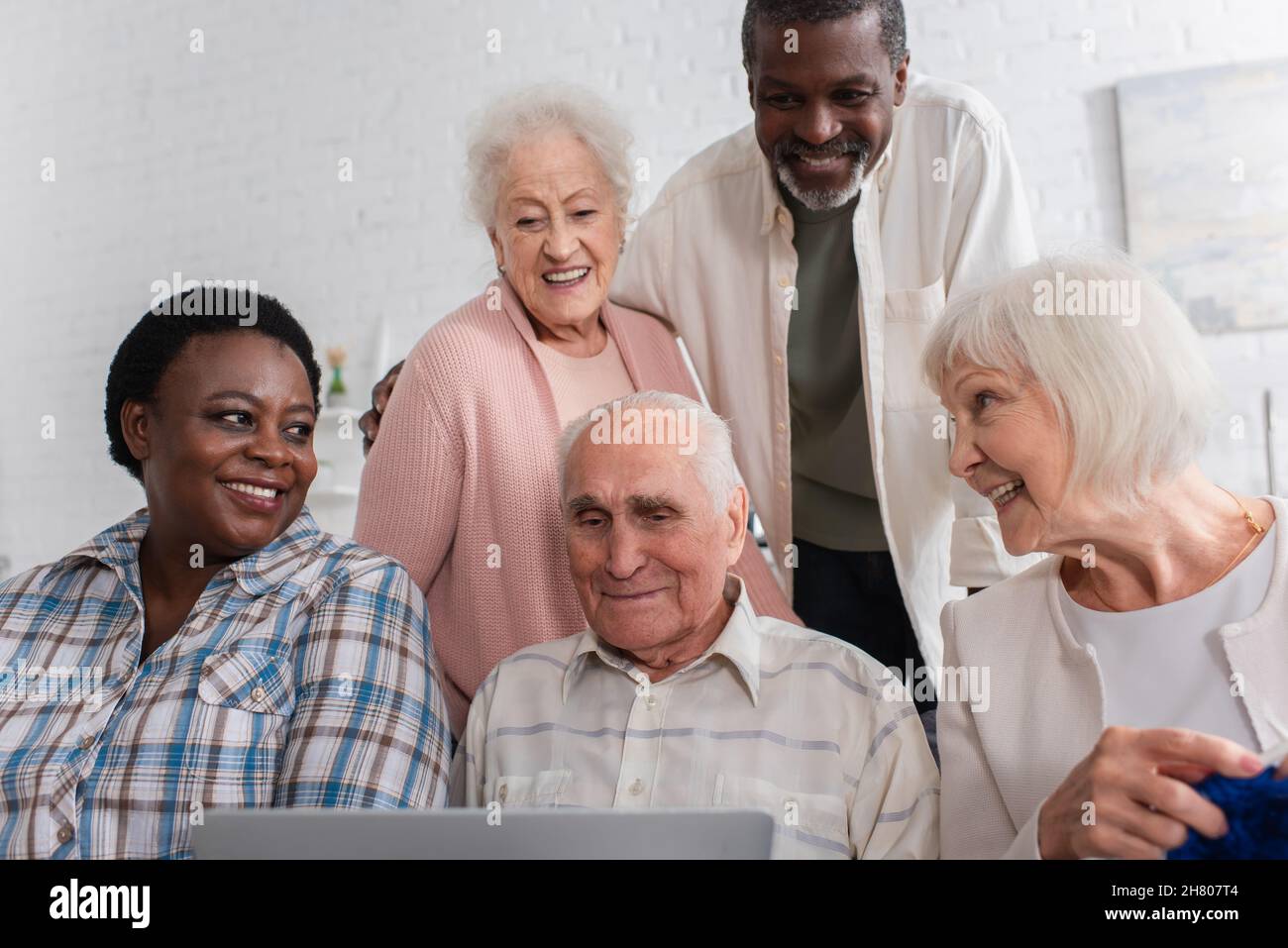 Felici pensionati multietnici con filo e notebook che trascorrono tempo in casa di cura Foto Stock