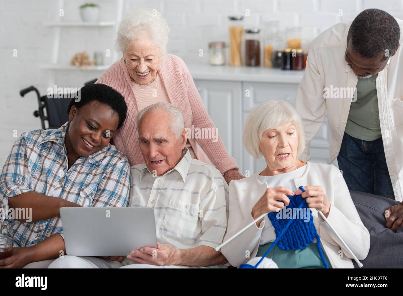 Anziani pensionati interrazziali che trascorrono tempo con filati e notebook in casa di cura Foto Stock