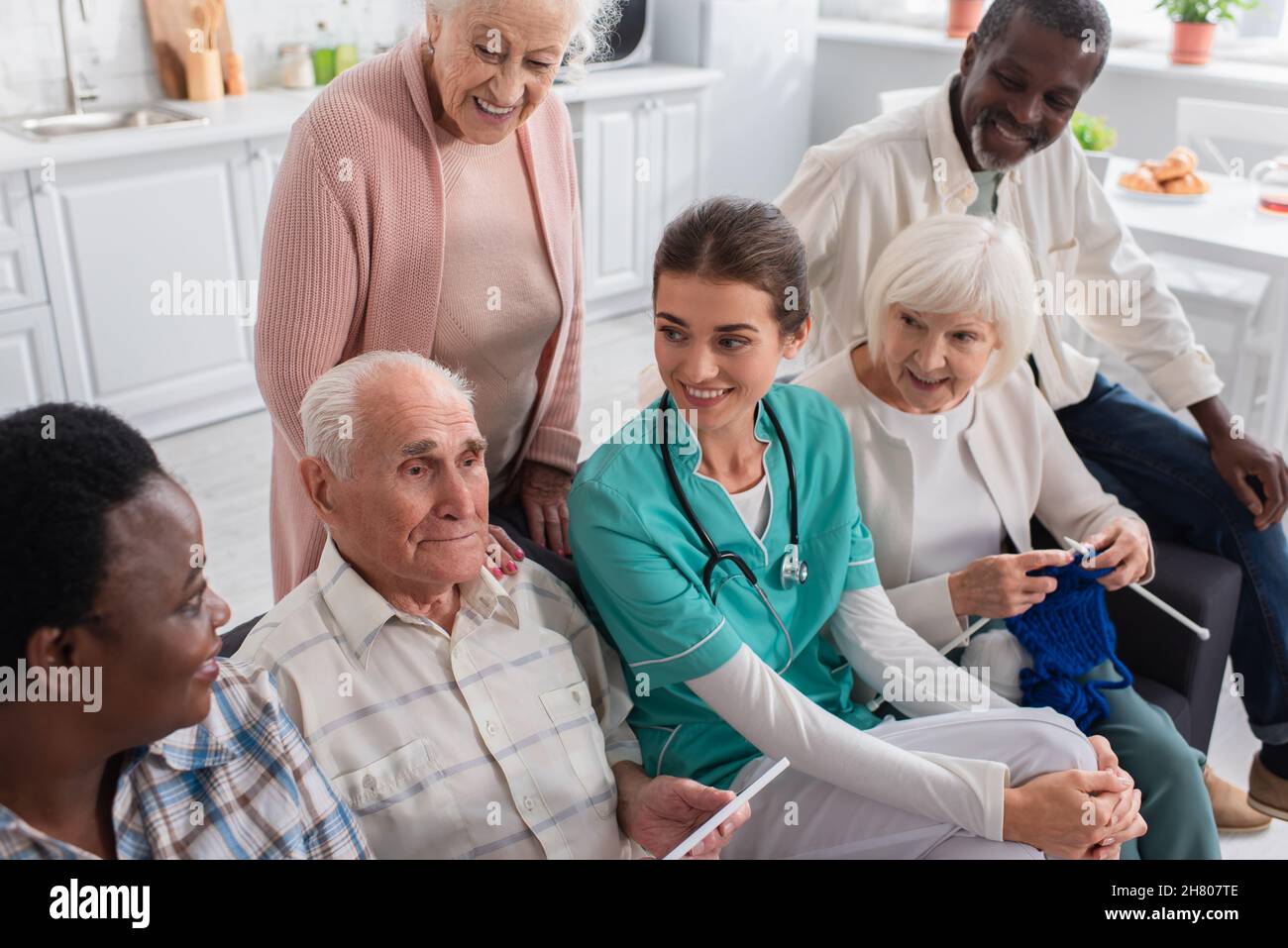 Uomo anziano che tiene il tablet digitale vicino all'infermiera e agli amici interrazziali in casa di cura Foto Stock