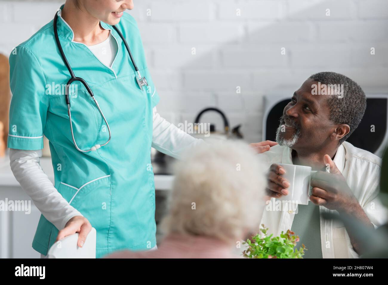 Uomo afroamericano che tiene la tazza vicino all'infermiera sorridente nella casa di cura Foto Stock