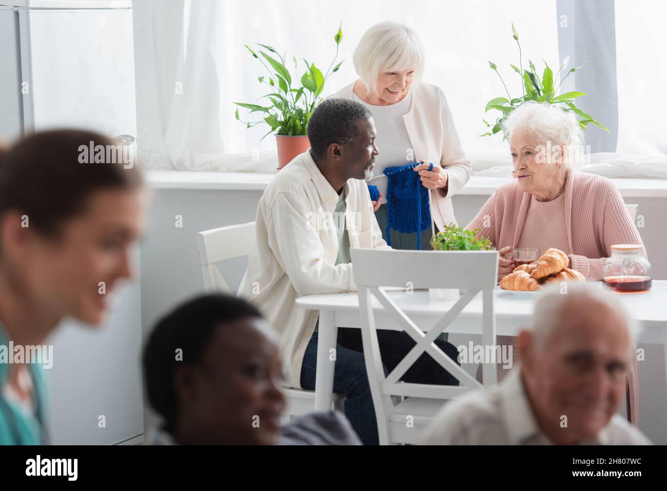 Sorridenti pazienti interrazziali con filati e tè che parlano in casa di cura Foto Stock