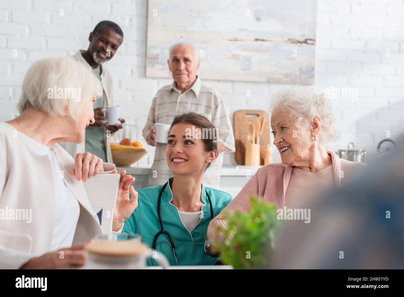 Giovane infermiera che passa il tempo con sorridenti pazienti interrazziali in casa di cura Foto Stock
