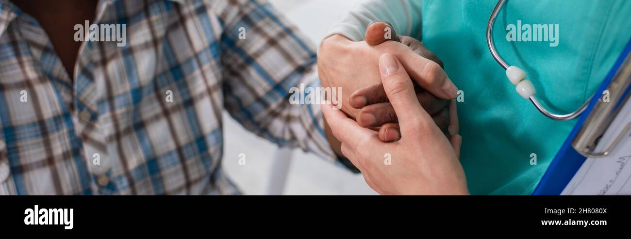 Vista croppata dell'infermiera che tiene la mano di un paziente afro-americano in casa di cura, banner Foto Stock