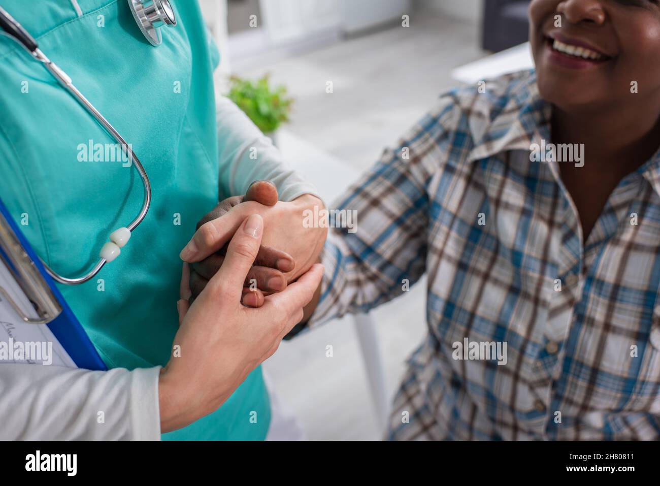 Vista croppata dell'infermiera con appunti che tengono la mano della donna afroamericana sorridente nella casa di cura Foto Stock