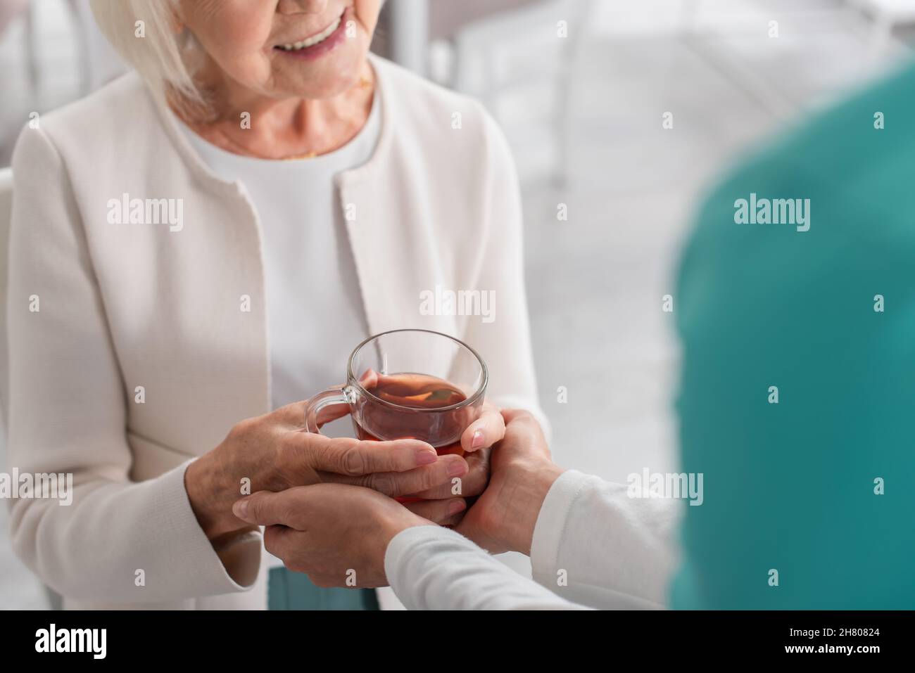 Vista ritagliata dell'infermiere che tiene le mani del paziente sorridente con il tè in casa di cura Foto Stock