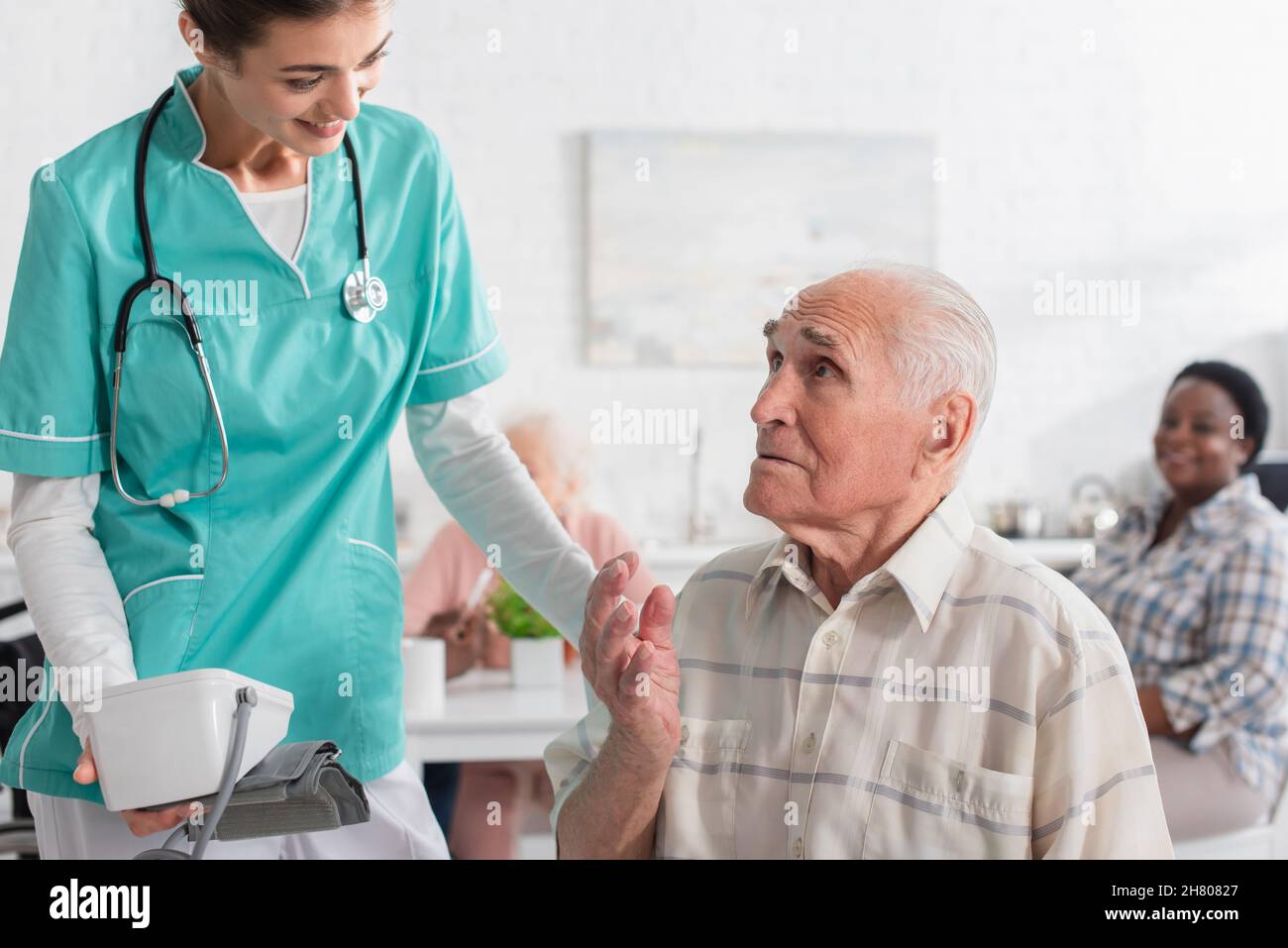 Infermiera sorridente che tiene il tonometro vicino a un paziente anziano in una casa di cura Foto Stock