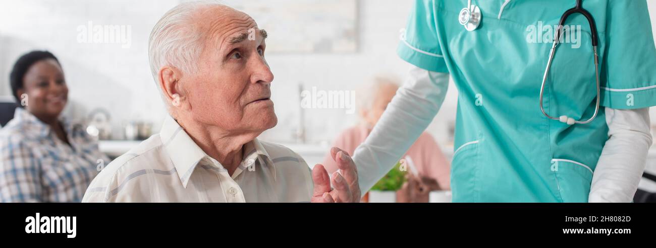 Uomo anziano che parla vicino infermiere in casa di cura, banner Foto Stock